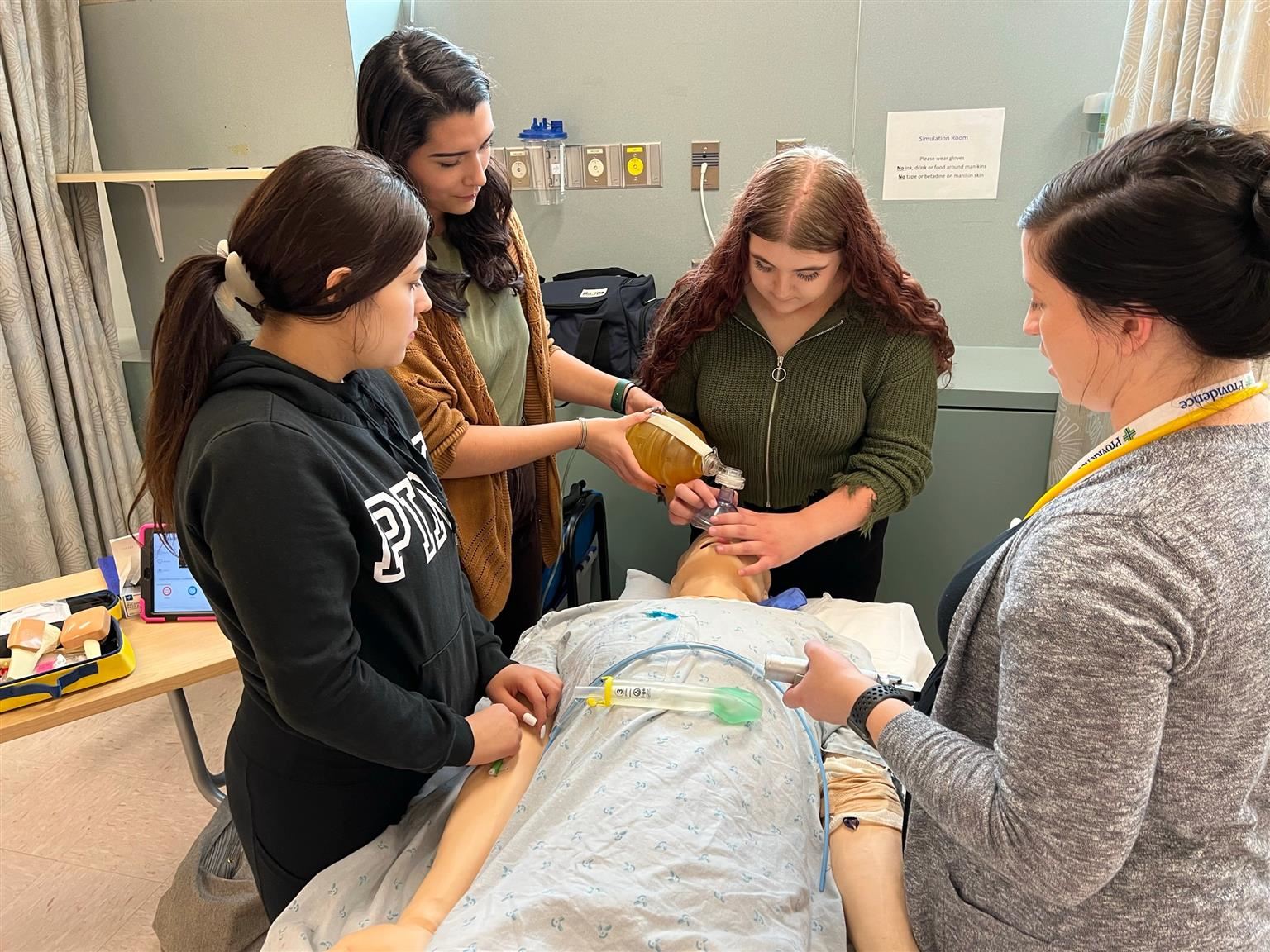 Students lean over a dummy in the sim lab.