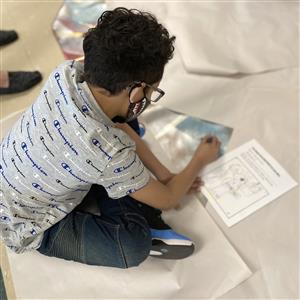 Kid sitting cross-legged drawing on canvas 