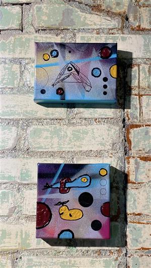 Two smaller canvas paintings hanging on a brick wall. 